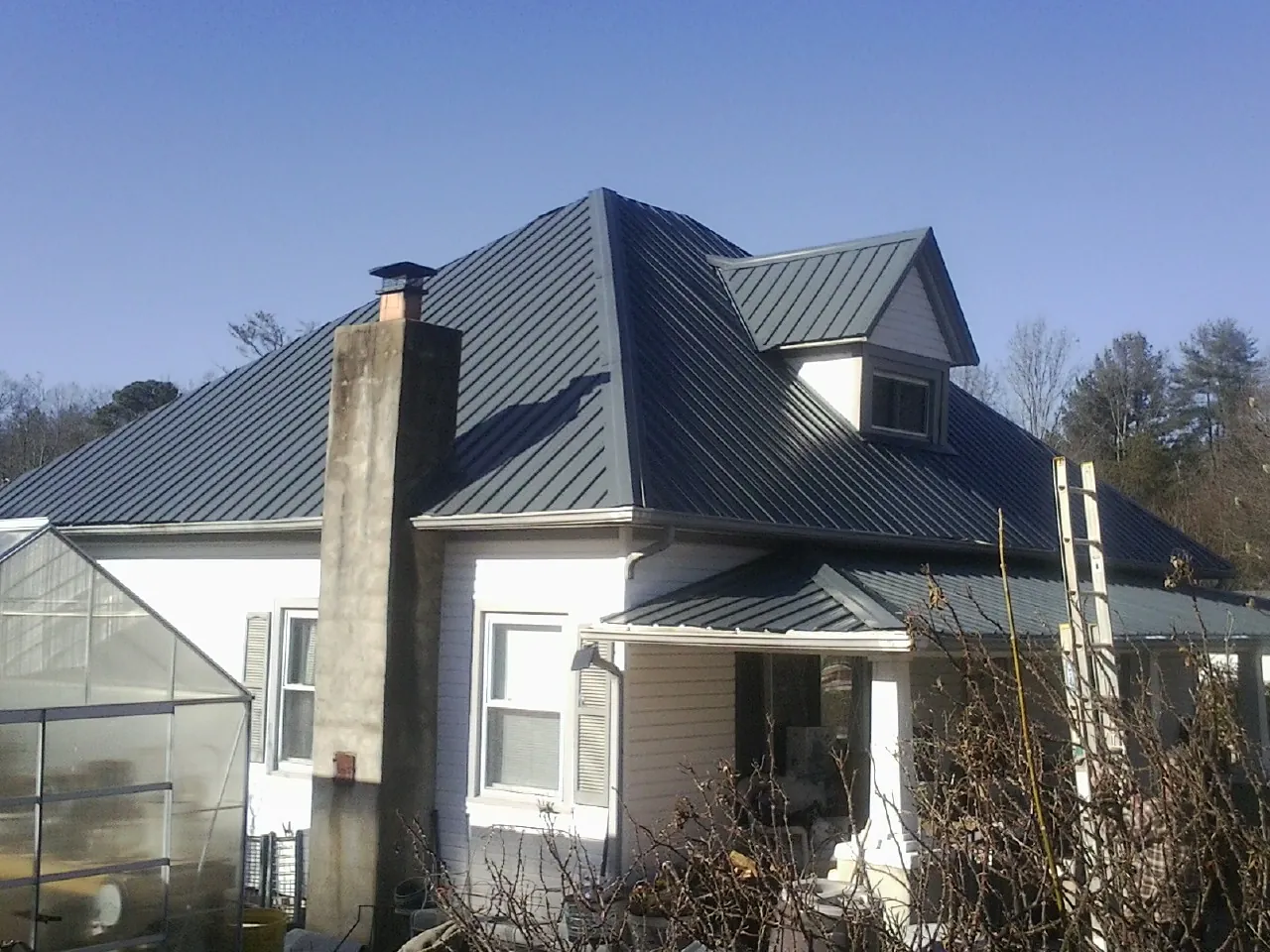 Dark blue standing seam metal roof on a white farmhouse with dormer — Slate & Tile Roof Repair by Roofing Brothers in Bellbrook