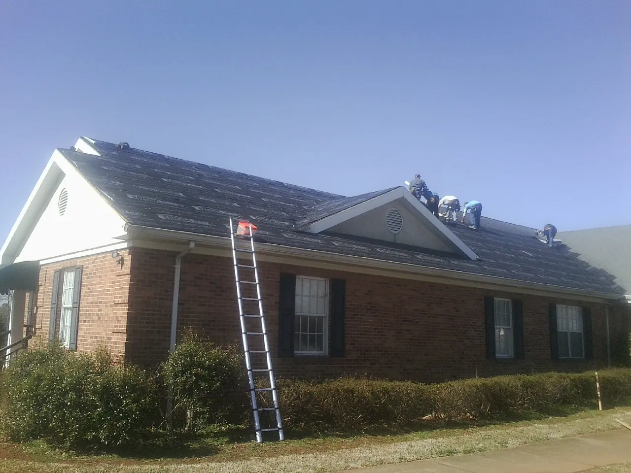 Crew tearing shingles off a brick ranch roof with a ladder set — Metal Roof Repair work by our crew in Bellbrook