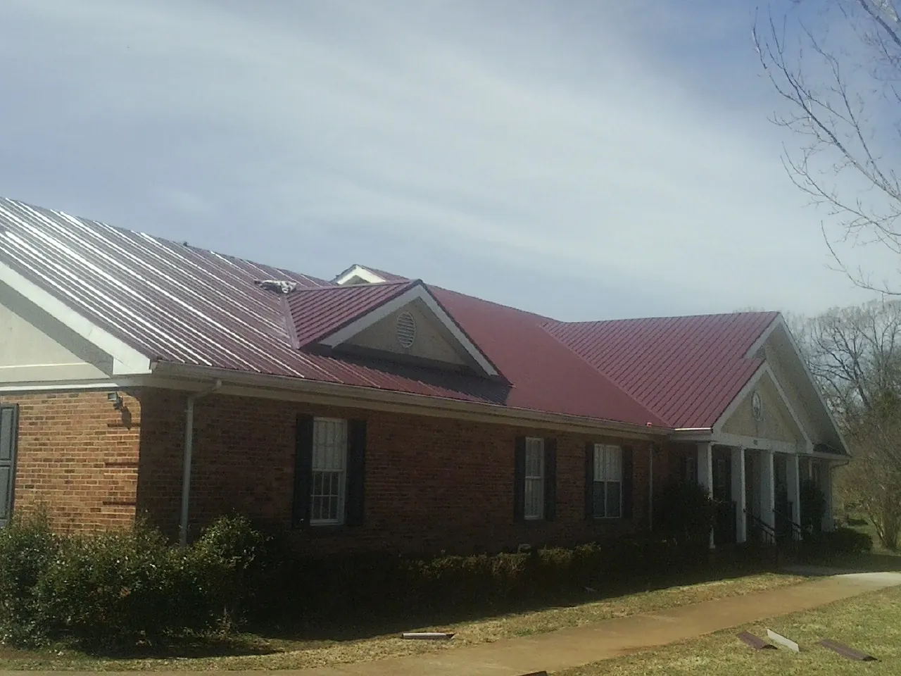 Red metal roof with gabled entries on a long brick building, from a Hail Damage Roof Repair job in Bellbrook