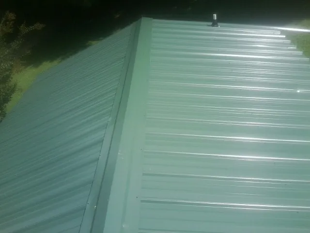 New green metal panels meeting at the ridge of a roof — Flat Roof Repair work by our crew in Bellbrook