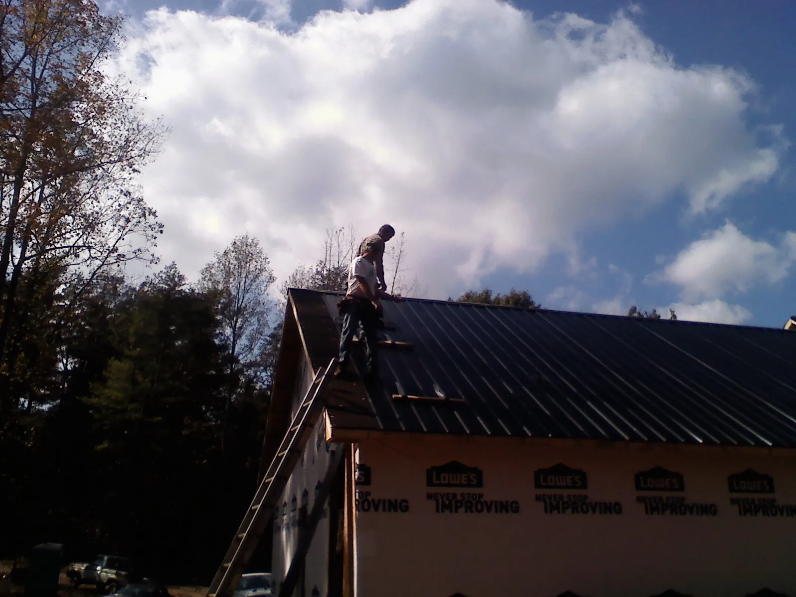 Roofer fastening dark metal panels high against a cloudy sky, from a Roof Inspection job in Bellbrook