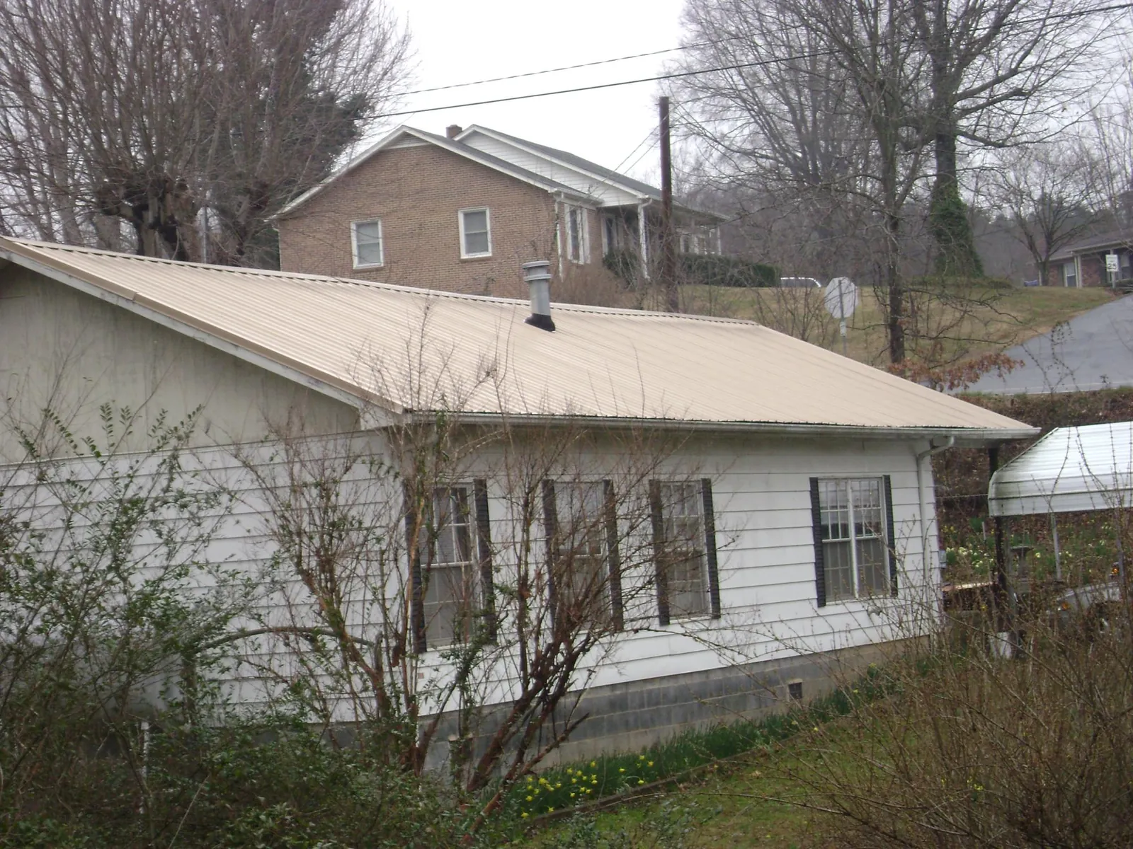 Tan metal roof on a white sided house set into a hillside — Commercial Roofing by Roofing Brothers in Bellbrook